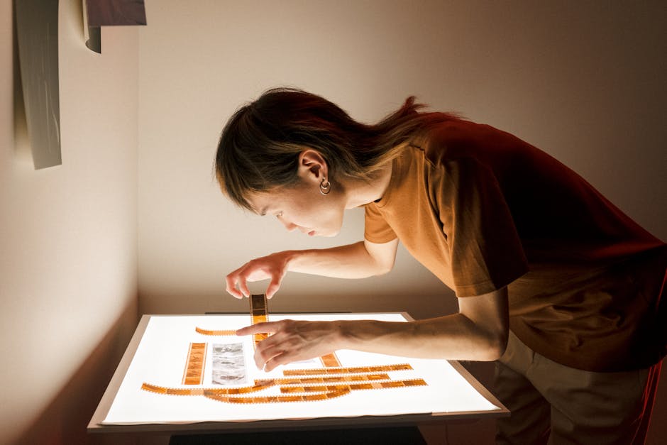 A photographer inspects film negatives on a light table in a dimly lit room.