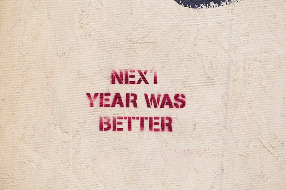 Rustic wall art with an inspirational message 'NEXT YEAR WAS BETTER' stenciled on a textured surface.
